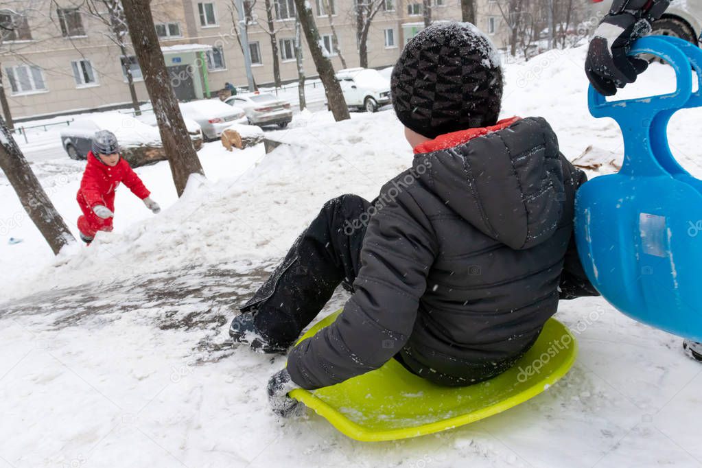 A boy of seven years old rides the slide , down the hill on green ice sled. Concept of winter activities, recreation and children's entertainment.
