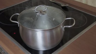 Sıcak bir kapak kaynar su indüksiyon camına bir tava seramik alarak yardım aşçı üst soba, buhar artar