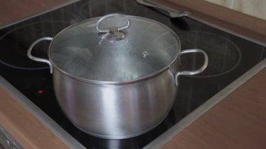Pişmemiş makarna kaynar su - indüksiyon cam seramik Ocak aşçı top, kaynar su ile bir tavada bir sıcak kapak alarak bir el koyarak Buhar gider
