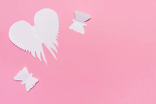 White angel wings and butterflies cut of paper on pink background, easter and spring concept with copy space.