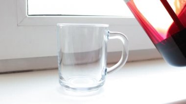 Kırmızı ebegümeci çayı üzerinde bir pencere pervazına Şeffaf şeffaf cam fincan içine dökme yakın çekim