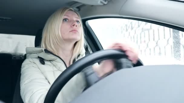 年轻的金发碧眼的女人穿着冬衣 在城市的冬路上开车 — 图库视频影像