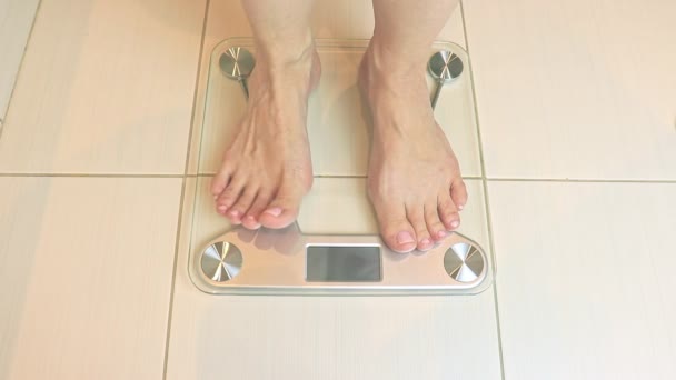 Жінка голими ногами стоїть на вагах і зважується у ванній - концепція дієти та схуднення — стокове відео