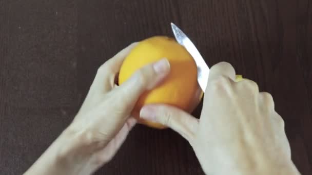 Kvinnans hand är peelingan orange på en trä bakgrund. enklaste och snabbaste sättet — Stockvideo