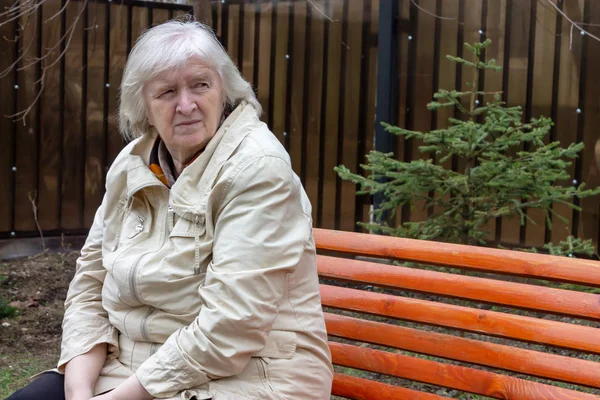 Portrait of the grey haired sad elderly woman sitting on the the park bench.