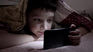 Rahatlatıcı ve izlerken bir yatakta evde, video akıllı battaniyenin altında karanlıkta yatarken bir çocuk