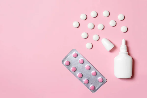 White plastic nasal spray and tablets for flu treatment on pink background with copy space - cold treatments and medicines concept