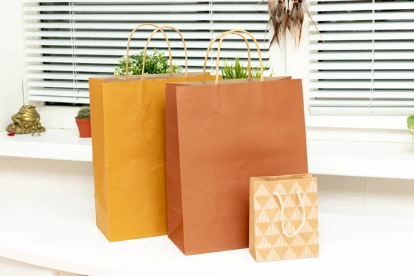 Bolsas de compras de papel marrón y beige en habitación moderna y luminosa con plantas verdes en un alféizar de la ventana, compras para crear comodidad en el hogar — Foto de Stock