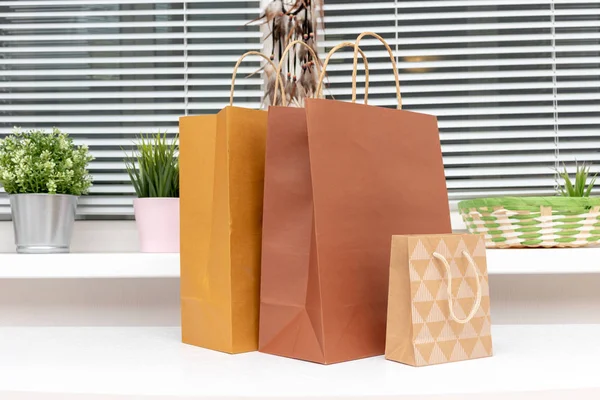 Bolsas de compras de papel marrón y beige en habitación moderna y luminosa con plantas verdes en un alféizar de la ventana, compras para crear comodidad en el hogar — Foto de Stock