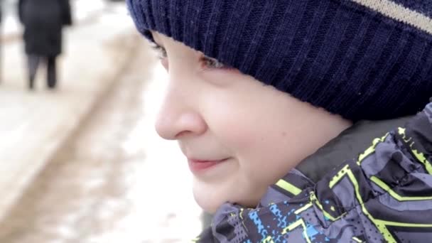 Primer plano retrato de un hermoso niño preadolescente con ojos increíbles sentado en un banco en el parque en invierno — Vídeos de Stock