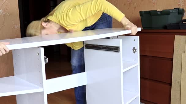 Женщина, устанавливающая новую белую мебель, кладет столешницу на новый полусобранный туалетный столик — стоковое видео