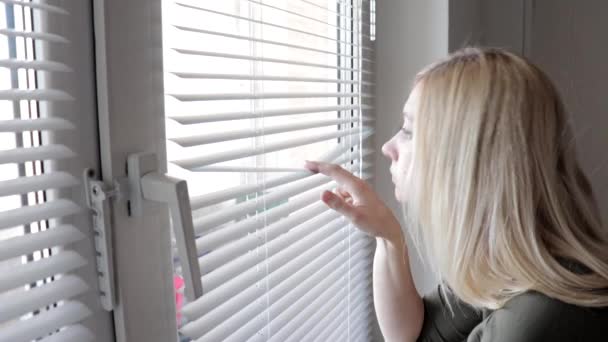 Nyfiken ung kvinna spionerar, kikar igenom mörkarna i hennes hem — Stockvideo