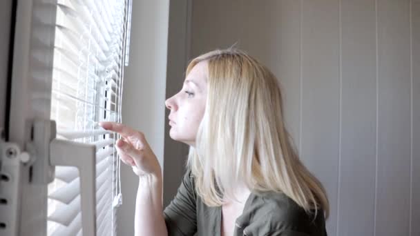 Nieuwsgierige jonge vrouw spionage, gluren door de blinds in haar huis — Stockvideo