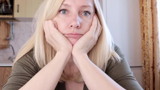 Portret van een trieste en verveelde jonge blonde vrouw zit in de keuken, verdriet en depressie concept — Stockvideo