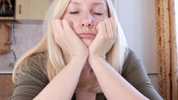 Portrait d'une jeune femme blonde triste et ennuyeuse assise dans la cuisine, concept de tristesse et de dépression — Video