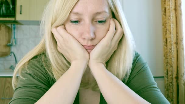 Портрет грустной и скучающей молодой блондинки, сидящей на кухне, печали и депрессии — стоковое видео