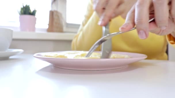 Mujer sentada junto a la mesa, comiendo un omlet con un folklore y un cuchillo y tomando café o té para desayunar en casa o restaurante — Vídeos de Stock