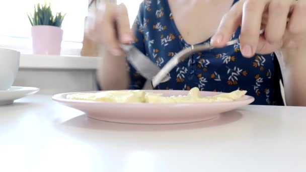 Жінка, сидячи за столом, їсть омлет з народним ножем і п'є каву або чай на сніданок вдома або ресторані — стокове відео