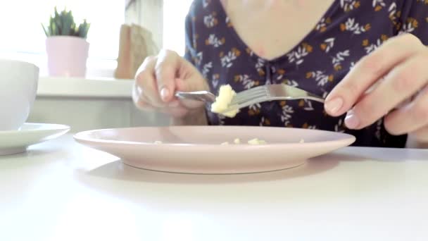 Mujer sentada junto a la mesa, comiendo un omlet con un folklore y un cuchillo y tomando café o té para desayunar en casa o restaurante — Vídeo de stock