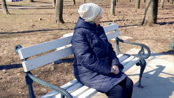 Portréja egy magányos depressziós idős nő ül egy padon a városi parkban kora tavasszal a napsütéses nap-apátia, a depresszió és a pszichológia egy idős emberek koncepció — Stock videók