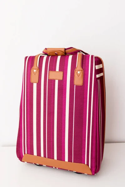 Red and white striped luggage bag on white background, minimal travel concept