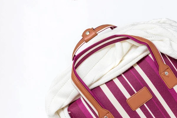 Red and white striped luggage bag with a knitted sweater on it , white background, minimal travel concept with copy space