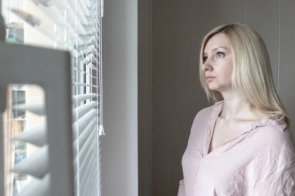 Sad apathetic lonely woman looking through a window at home or hotel, divorce, depression and apathy concept — Stock Photo, Image