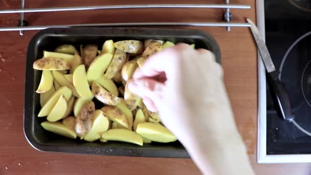 Female hand adding salt and spices to rustic potato pieces in frying pan or baking sheet — Stock Video