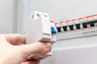 Arka planda, devre kesicili elektrik kontrol panelinde, evde otomatik elektrik anahtarları ile yeni otomatik anahtar ve bulanık elektrik kalkanı tutan el
