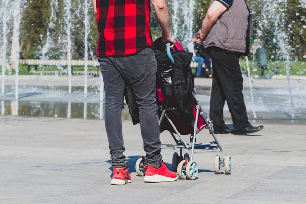 Solo padre soltero hipster en camisa a cuadros rojo y negro con un cochecito caminando en el parque de la ciudad — Foto de Stock