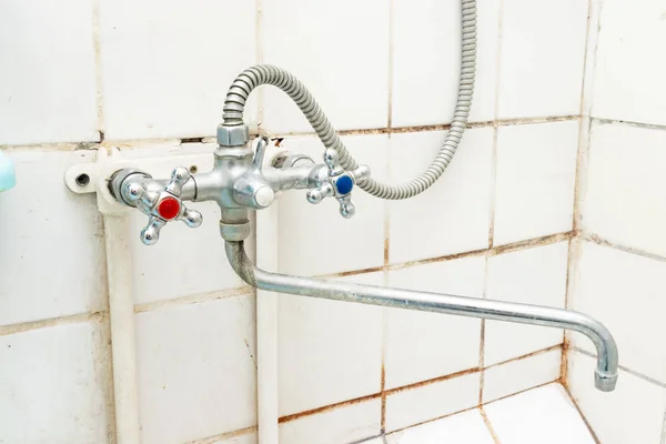 Dirty old faucet with limescale or lime scale on it, dirty calcified and rusty shower mixer tap and hose, moldy tiles on background. Mixer should be cleaned or replaced