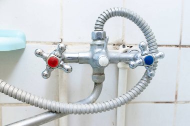 Üzerinde kireç veya kireç pulu olan eski kirli musluk, kirli kireçlenmiş ve paslı duş karıştırıcı musluk ve hortum, arka planda küflü fayanslar. Karıştırıcı temizlenmeli ya da değiştirilmeli
