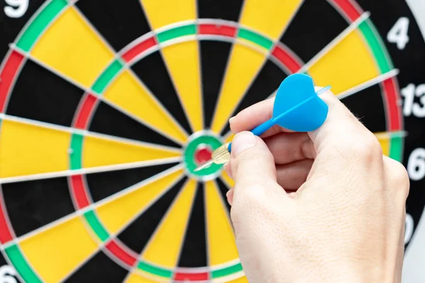 A hand holding a blue dart ready to throw it to a dartboard target, strategy and skill in business concept