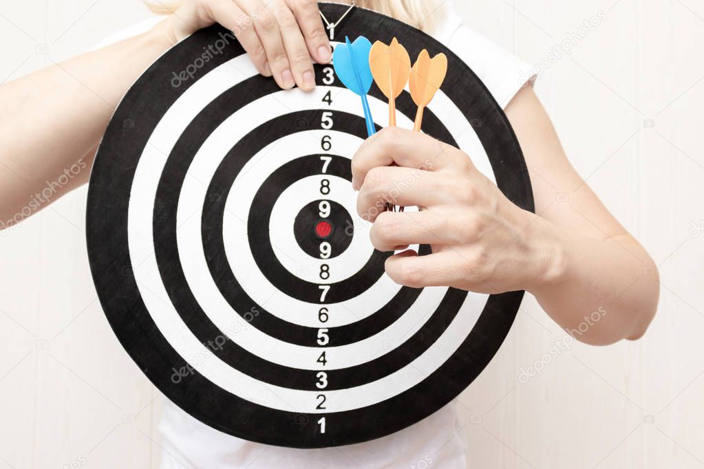 Woman holding a dart board and darts in hands close up, aiming and targetting in business and life concept