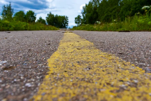 Yellow solid line, grunge road marking on asphalt close up with rural landscape on background — Stock Photo, Image