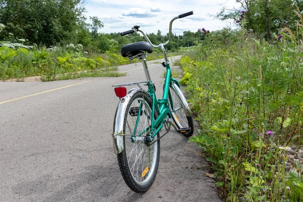 Зеленый велосипед, припаркованный на загородной дороге с зеленой травой на обочине, концепция велосипедного путешествия — стоковое фото