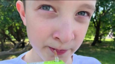Genç bir preteen kafkas çocuk yaz şehir parkında oturan ve kağıt suyu paketi bir saman ile suyu içme, yakın görünümü, paket fastfood kavramı