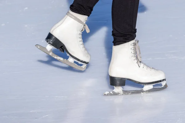 Ice skating, woman legs wearing white leather skates, training on a frosen snowy skating rink in winter close up