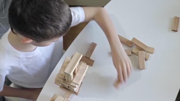 Ein kaukasischer Junge, der aus Holzklötzen einen Turm baut, ein Kind, das Spiele spielt, um körperliche und geistige Fähigkeiten und Unterhaltung zu üben — Stockvideo