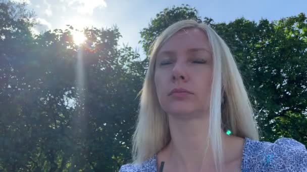 Genç sarışın beyaz beyaz kadın yaz şehir parkında bankta oturan ve tek kullanımlık kağıt paket fincan bir saman kullanarak kahve içme — Stok video