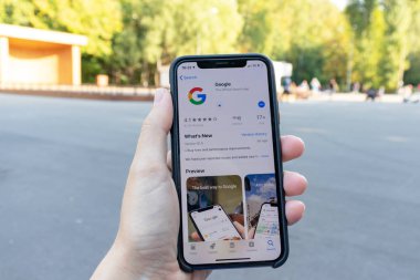 Moskova, Rusya - 01 Eylül 2019: Ekranda google uygulama simgesi olan bir akıllı telefon el tutuyor. Oyun pazarında Google uygulama simgesi, arka planda şehir parkı
