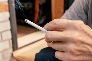 Bir sürü kül, kötü habbit ve nikotin bağımlılığı kavramı ile parmaklarında ışıklı bir sigara tutan adam