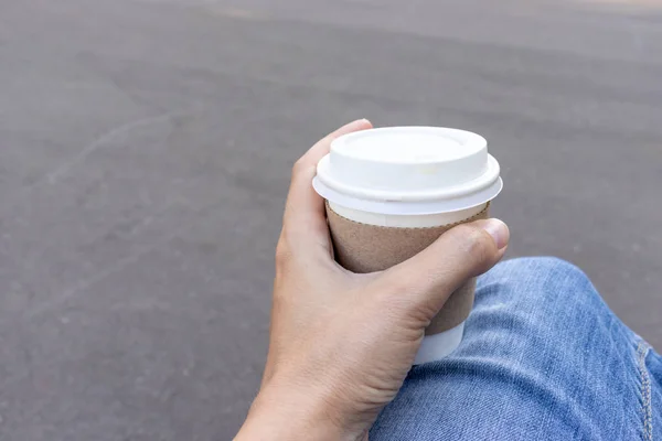 Woman sitting on a bench outdoor and holding a kraft disposadle paper cup of coffee with a white cup in hand — Stock Photo, Image