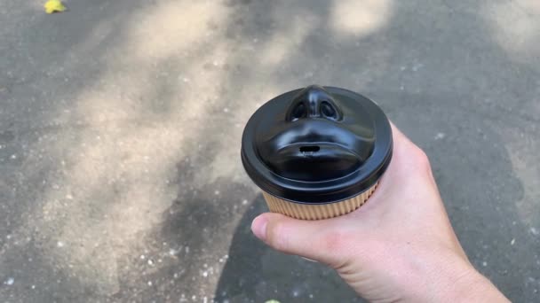 Uma mão segurando uma xícara de café descartável com um copo de forma de rosto humano preto, estilo de vida urbano e café em movimento — Vídeo de Stock