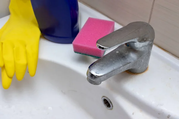 Чистящие средства, перчатки и губка для мытья грязного крана с лимескалем, кальцинированный водопроводный кран с лаймовой шкалой на раковине в ванной комнате — стоковое фото