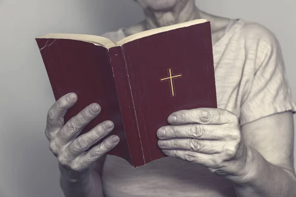 Mujer mayor sosteniendo una vieja y santa Biblia en las manos, anciana sosteniendo el Nuevo Testamento y orando — Foto de Stock