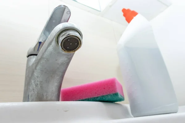 Чистящие средства, средства и губка для мытья грязного крана с лимескалем, кальцинированный кран воды с лаймовой шкалой на умывальнике в ванной комнате — стоковое фото