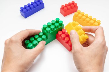 Renkli oyuncak plastik tuğlalardan inşa edilen eller, beyaz arka plan üzerine inşa edilen bloklar