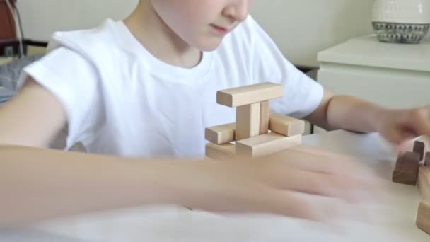 Ein kaukasischer Junge, der aus Holzklötzen einen Turm baut, ein Kind, das Spiele spielt, um körperliche und geistige Fähigkeiten und Unterhaltung zu üben — Stockvideo