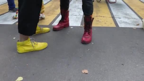 Piernas y pies de payasos vistiendo coloridas botas amarillas y rojas divertidas, jugando entre sí en el camino de asfalto — Vídeo de stock